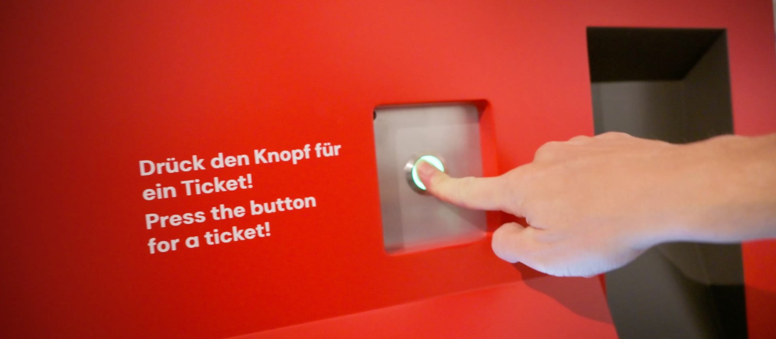 Hand drückt auf leuchtenden Knopf mit der Aufschrift „Drück den Knopf für ein Ticket!“: