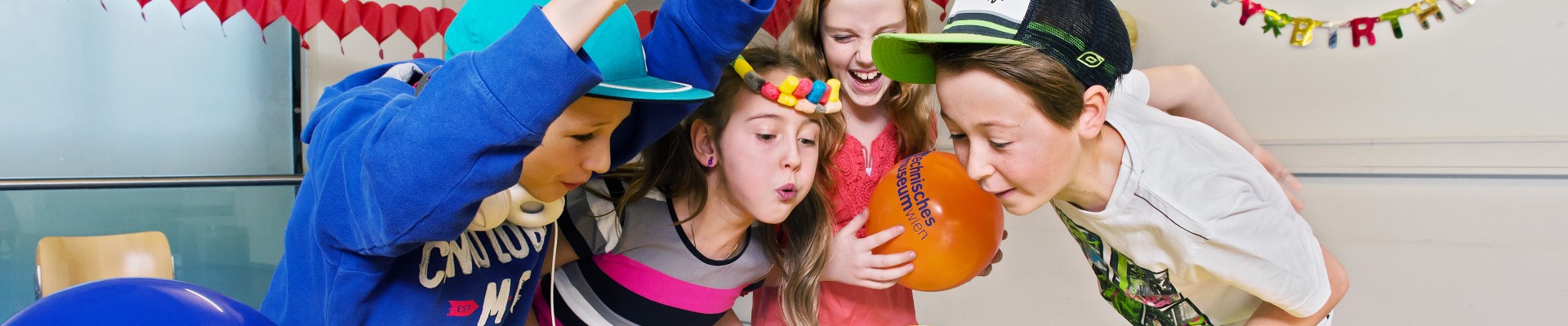 Children are celebrating a birthday party in the partyroom with a lot of decoration and a cake: 