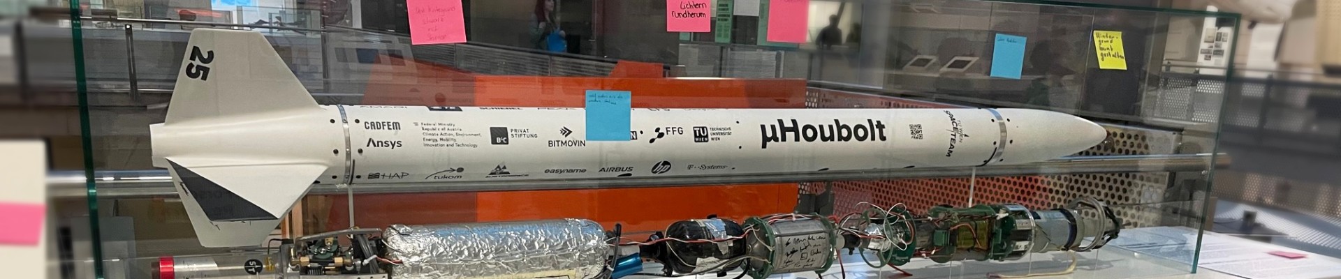 Ein Modell einer Rakete in einer Vitrine mit mehreren bunten Haftnotizen an der Vitrine und am Sockel, in einer Museumsausstellung mit der Aufschrift "Raketen.": Rückmeldungen zur und Vorschläge für die Raketenvitrine 