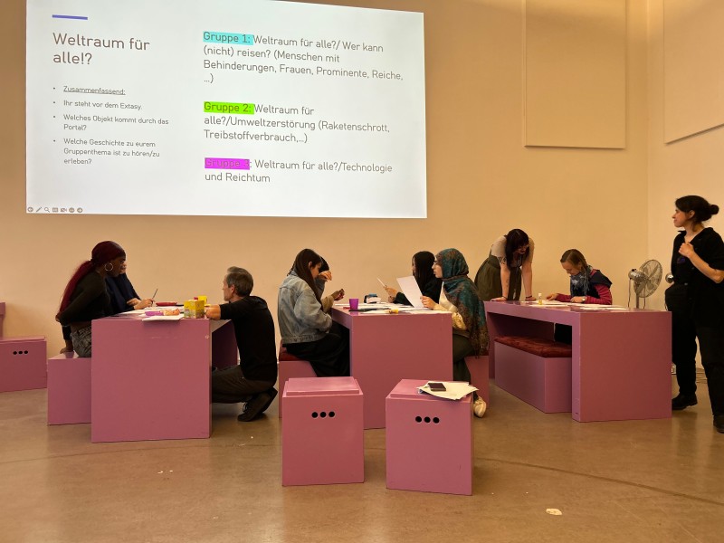 Young people work in groups at tables in front of a projected question “Space for all!?” at the Technisches Museum Wien.: Time to reflect: the Planet Hunters are considering how space can become more accessible for everyone and what other obstacles exist.