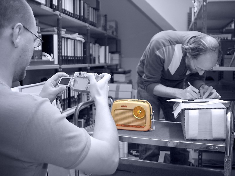 : Schwarz-weiß Foto: Museumsmitarbeiter bei der Arbeit mit einem gelben Transistorradio