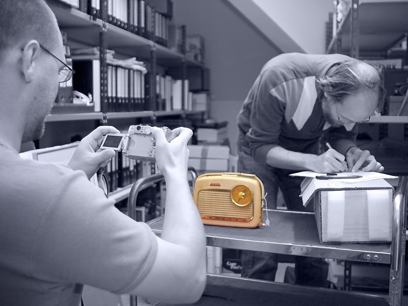 Black and white photo: museum employee working with a yellow transistor radio: 