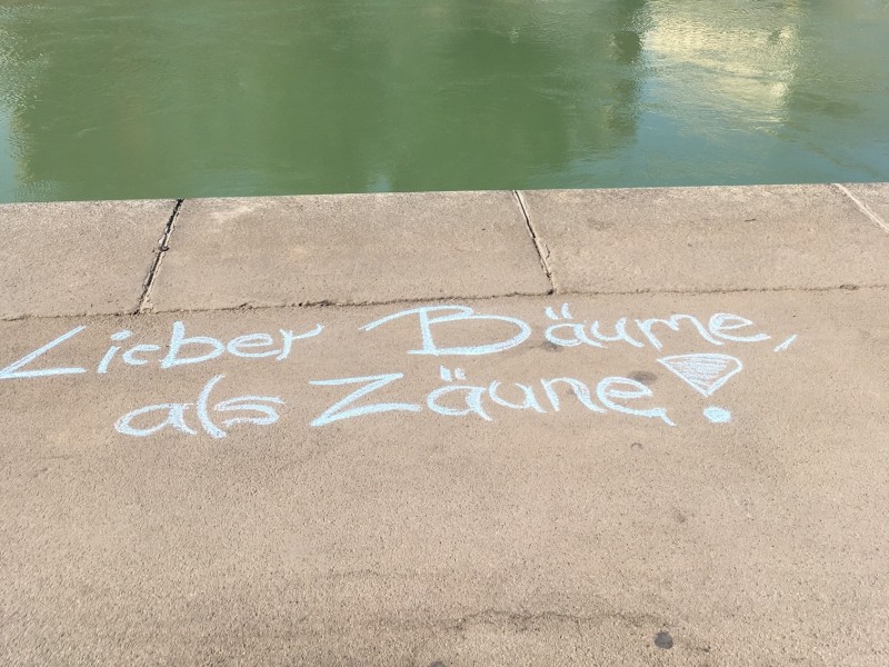 : Wiener Donaukanal: Kreideschrift am Asphalt "Lieber Bäume als Zäune"