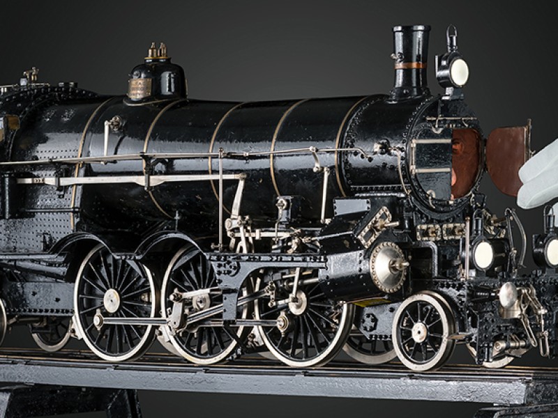Detailaufnahme eines historischen Lokomotivmodells mit geöffneter Rauchkammertür, gehalten von einer Hand mit weißem Handschuh: 