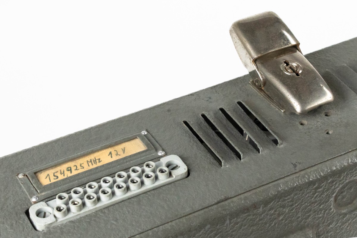 Detailansicht eines historischen Funkgeräts mit Beschriftung „154,925 MHz 12 V“, Anschlussbuchse und Metallklammer: ... und nach der Reinigung (Inv.-Nr. 114.106)