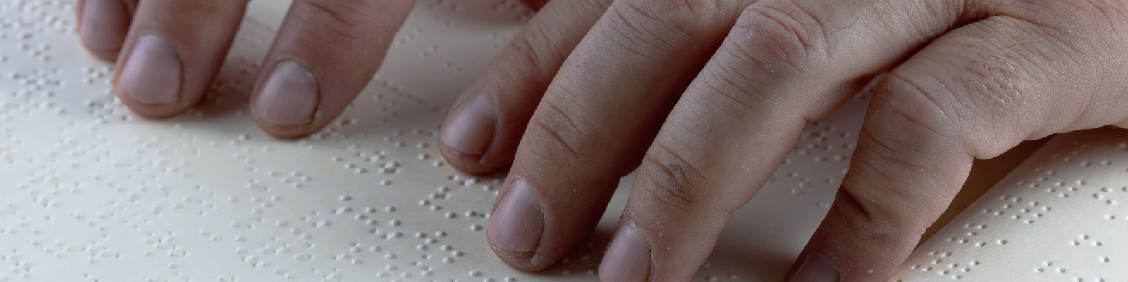 Hände ertasten einen Text in Braille-Schrift.