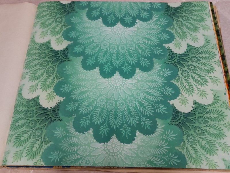 Gesamtaufnahme einer Musterbuchseite mit ornamentaler Buntpapiergestaltung in Grün- und Türkistönen. Das symmetrische Muster besteht aus stilisierten Blatt- und Farnmotiven, die sich in großen, fächerförmigen Formen über die gesamte Seite wiederholen: Abb. 4: Gesamtaufnahme der beprobten Seite eines „Buntpapier-Musterbuchs“ (Inv.-Nr. 61125)