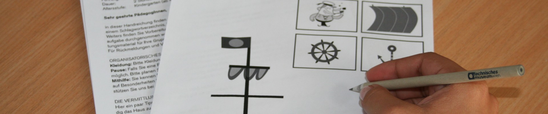 : Kinderhand beim Ausfüllen eines Papierbogens, auf dem die Illustration eines Schiffes abgebildet ist.