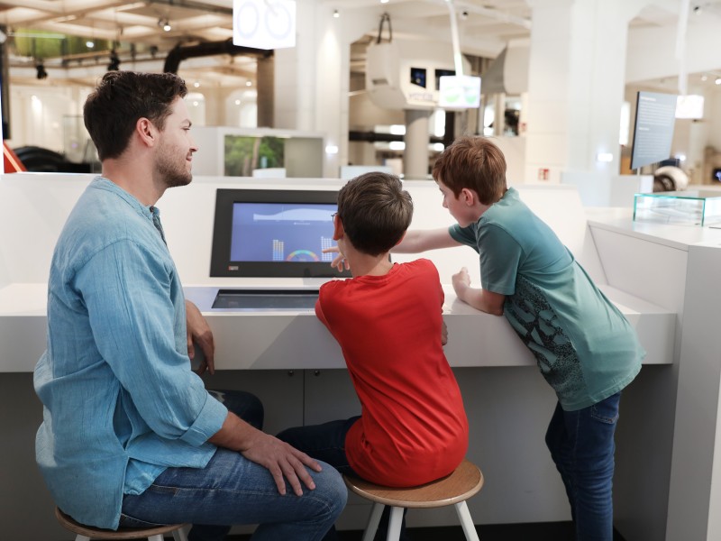 Vater mit Kindern vor einem Monitor in der Ausstellung "Energie": 