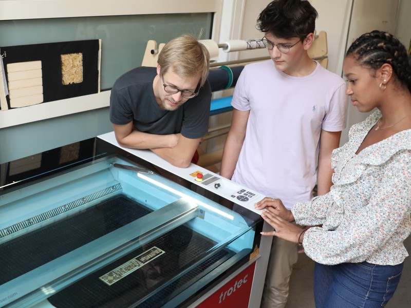 Three Teenagers look at the wood laser cutter in the TechLab