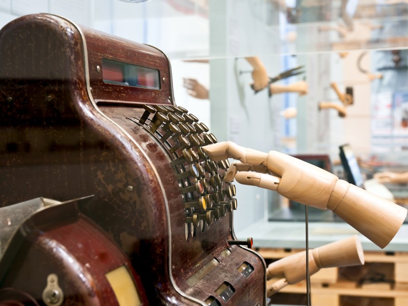 Das Modell einer Hand bedient eine historische Registrierkasse in der Ausstellung "In Arbeit" auf Ebene 3.: 