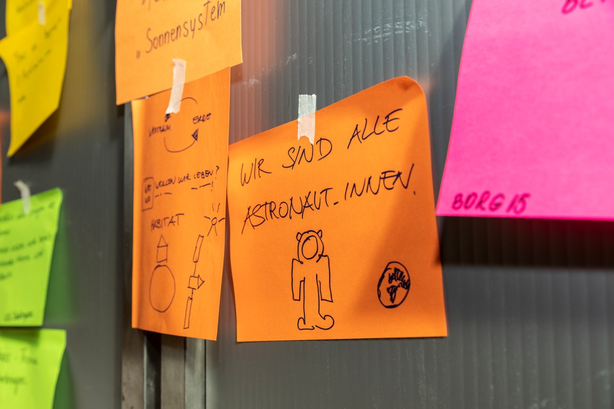 Ein Post-it mit Beschriftung "Wir sind alle Austronaut_innen"