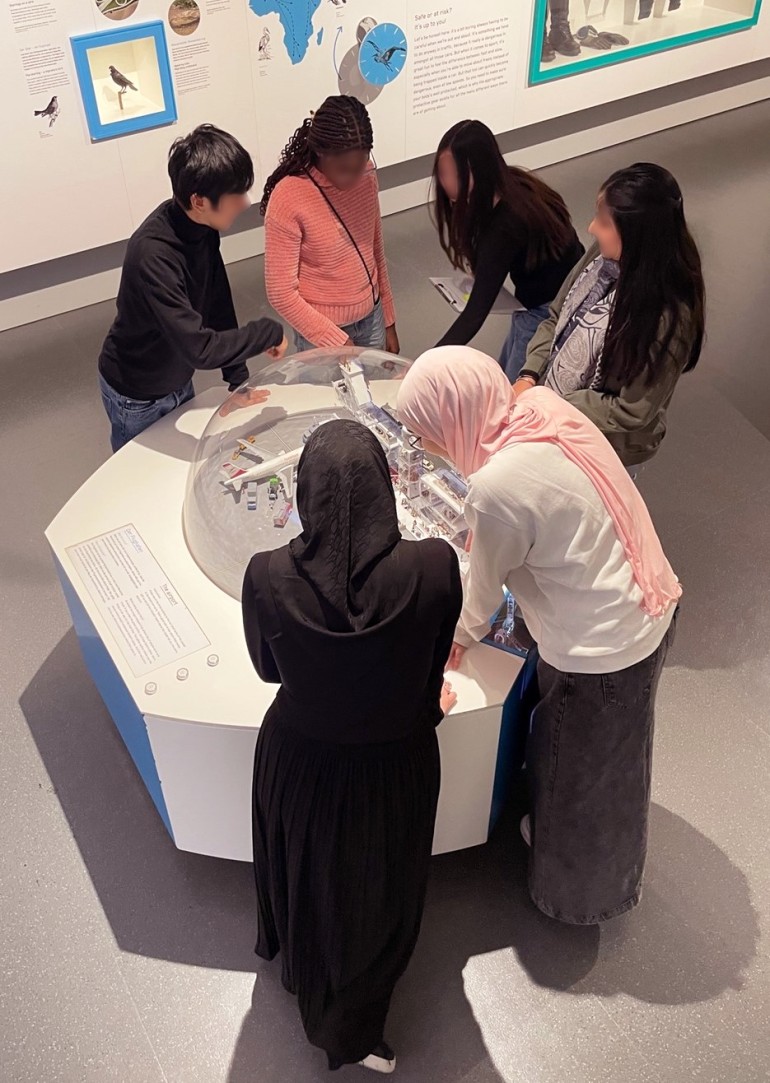 Eine Gruppe von Personen versammelt sich um ein kreisförmiges Exponat in einem Museum und interagiert mit einem Modell unter einer transparenten Kuppel.: Besuch in der Ausstellung <i>In Bewegung</i>. Inspiriert von aktuellen Hands-On-Objekten hat die MISSION CONTROL Überlegungen für eine künftige Ausstellung angestellt.