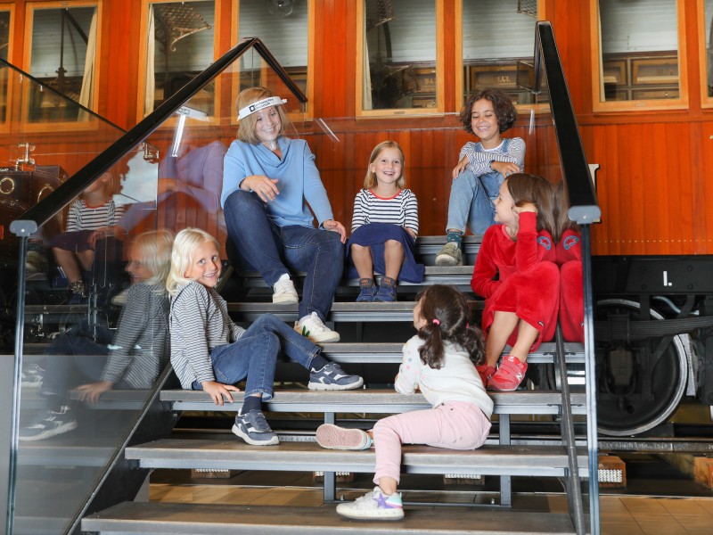 Children sit together with a tour guide on the stairs from Sisi´s Hofsalonwagen. It is part of the exhibition "Lok.Erlebnis" : 