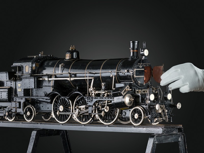 Detailaufnahme eines historischen Lokomotivmodells mit geöffneter Rauchkammertür, gehalten von einer Hand mit weißem Handschuh: