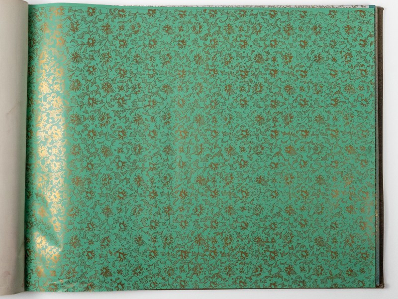 Gesamtaufnahme einer Musterbuchseite mit türkisfarbenem Buntpapier. Die Fläche zeigt ein dichtes, sich wiederholendes florales Rankenmuster mit goldfarbenen Blüten und Blättern, das die gesamte Seite bedeckt: Abb. 3: Gesamtaufnahme der beprobten Seite eines „Buntpapier-Musterbuchs“ (Inv.-Nr. 61101)