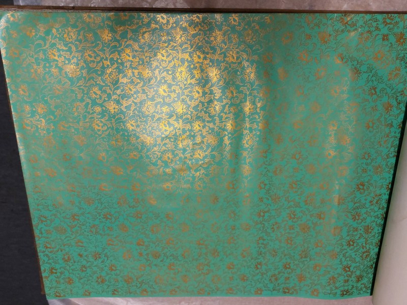 Gesamtaufnahme einer Musterbuchseite mit türkisfarbenem Buntpapier. Die Fläche zeigt ein dichtes, sich wiederholendes florales Rankenmuster mit goldfarbenen Blüten und Blättern, das die gesamte Seite bedeckt: Abb. 3: Gesamtaufnahme der beprobten Seite eines „Buntpapier-Musterbuchs“ (Inv.-Nr. 61101)