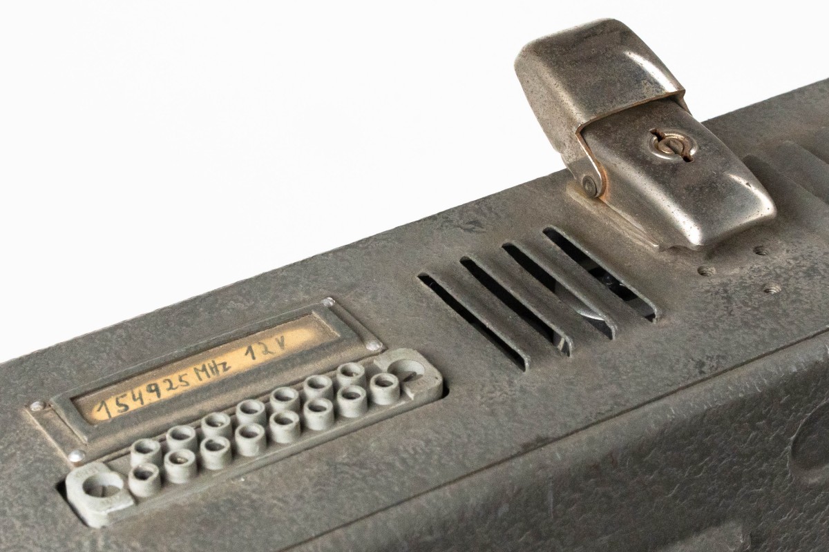 Detailansicht eines historischen Funkgeräts mit Beschriftung „154,925 MHz 12 V“, Anschlussbuchse und Metallklammer: Funksprechanlage vor ...