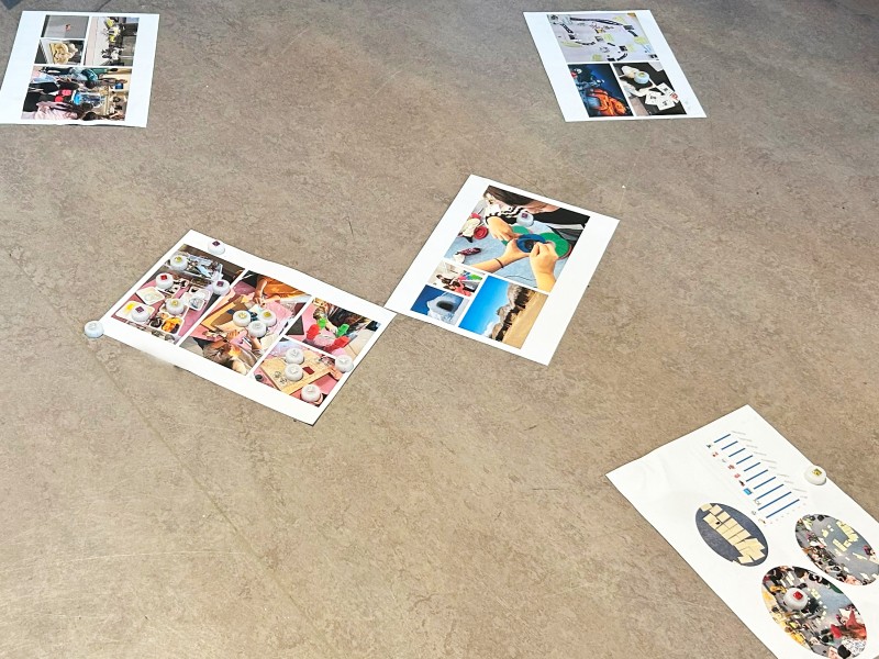 Various printed photo sheets are spread out on the floor, each featuring images of workshop activities and crafts, with small markers placed on them.: The students shared their feedback: What did they enjoy the most? What aspects of the workshop series would they have liked more of, and what less?