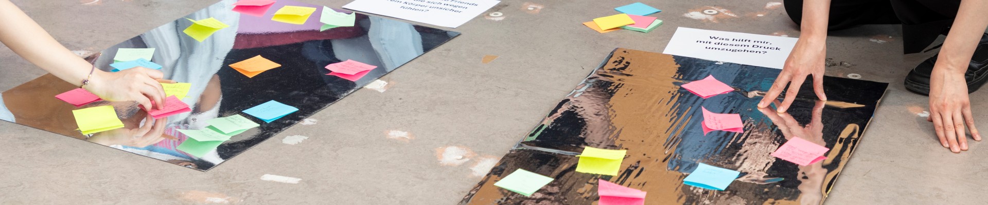 Teilnehmer setzen Post-It-Notizen auf Plakate mit Fragen zum Thema Körperbild und Stressbewältigung.: 