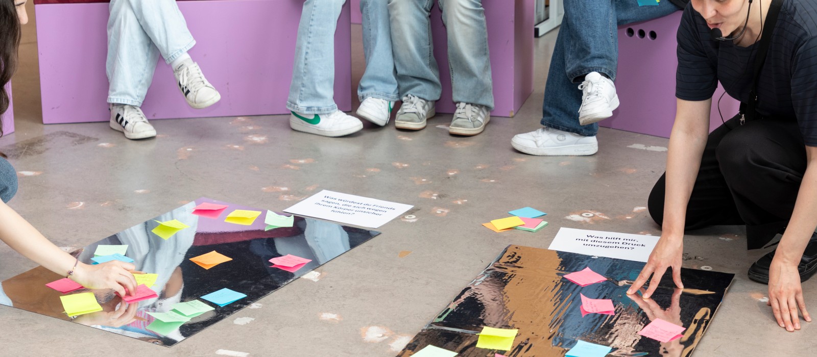 Teilnehmer setzen Post-It-Notizen auf Plakate mit Fragen zum Thema Körperbild und Stressbewältigung.: