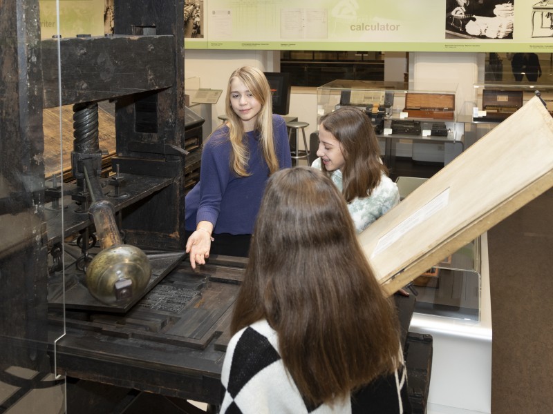 Young people stand in front of a historical printing press