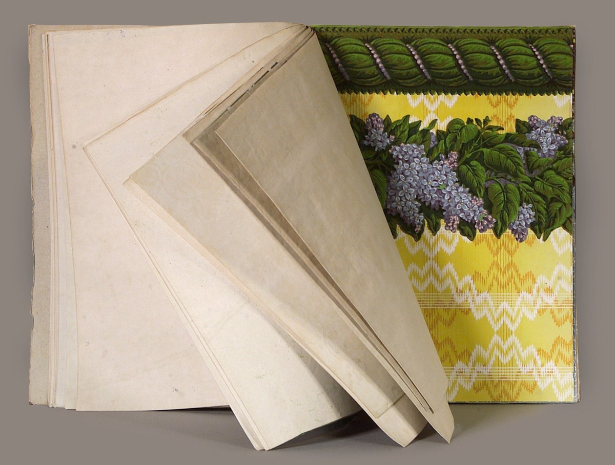 Historisches Tapetenmusterbuch mit aufgefächerten Seiten und sichtbar eingeheftetem Tapetenmuster mit floraler Bordüre.: Abb. 1: Einsicht in eines von vielen Tapetenmusterbüchern (Inv.-Nr. 36876)