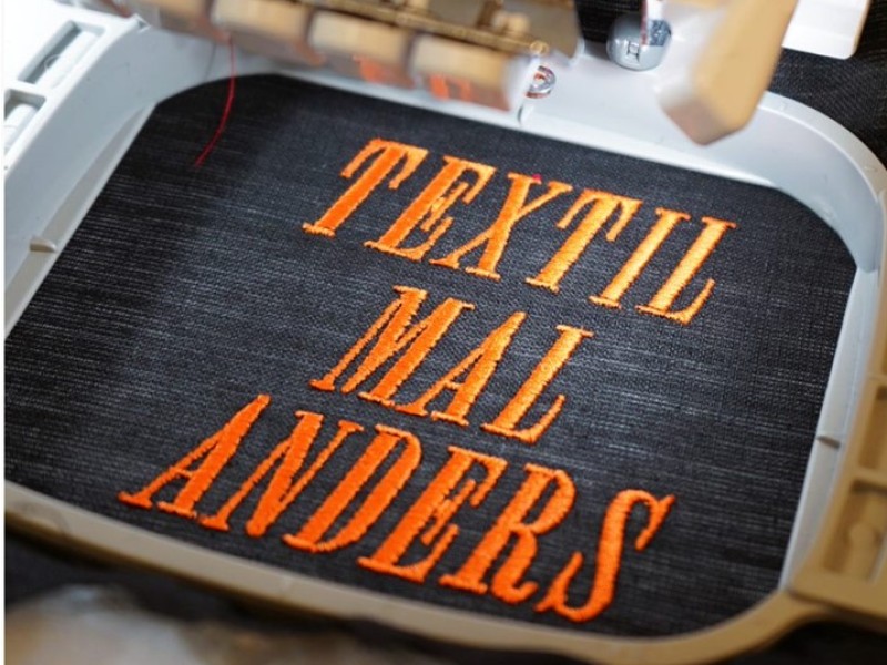 Mit der Stickmaschine besticktes Stück Textil mit der Aufschrift "Textil mal anders": Mit der Stickmaschine besticktes Stück Textil