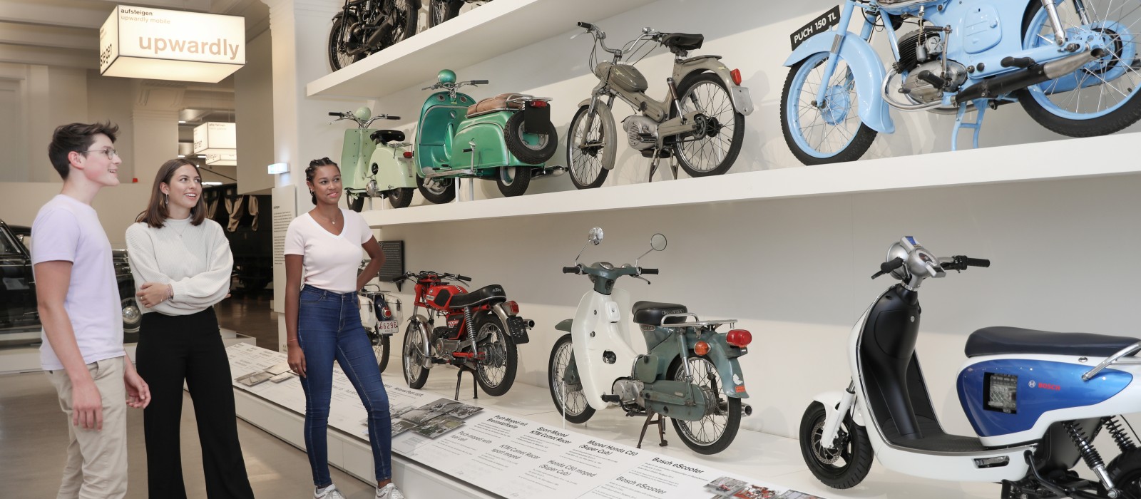 Eine kleine Gruppe Jugendlicher sieht sich in der Ausstellung "Mobilität" verschiedene Mopeds und Motorräder an. : 