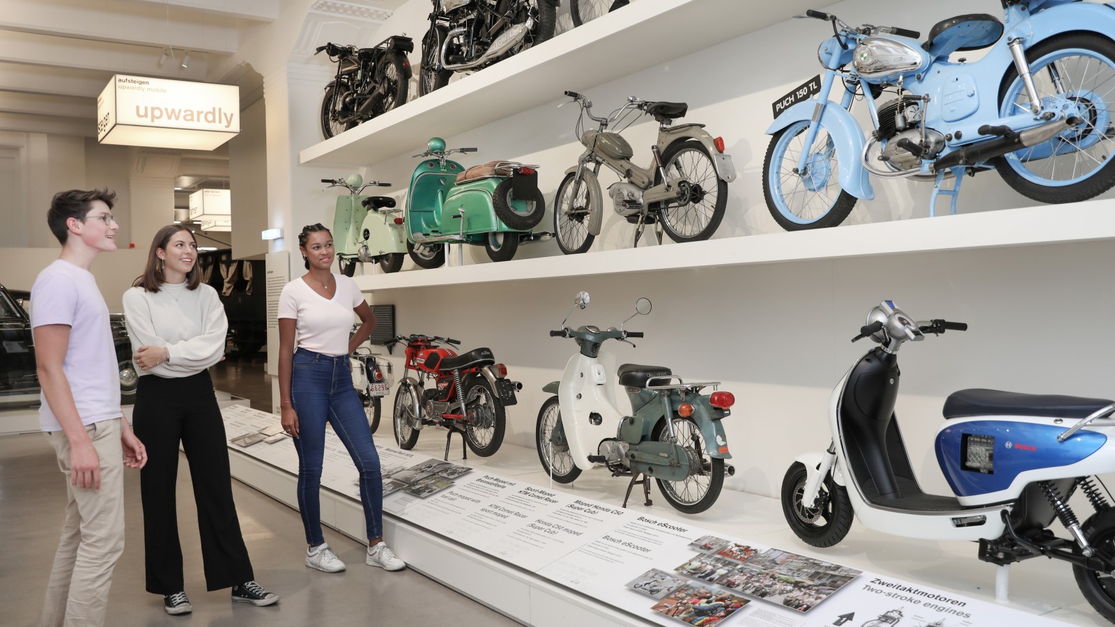 Eine kleine Gruppe Jugendlicher sieht sich in der Ausstellung "Mobilität" verschiedene Mopeds und Motorräder an. : 