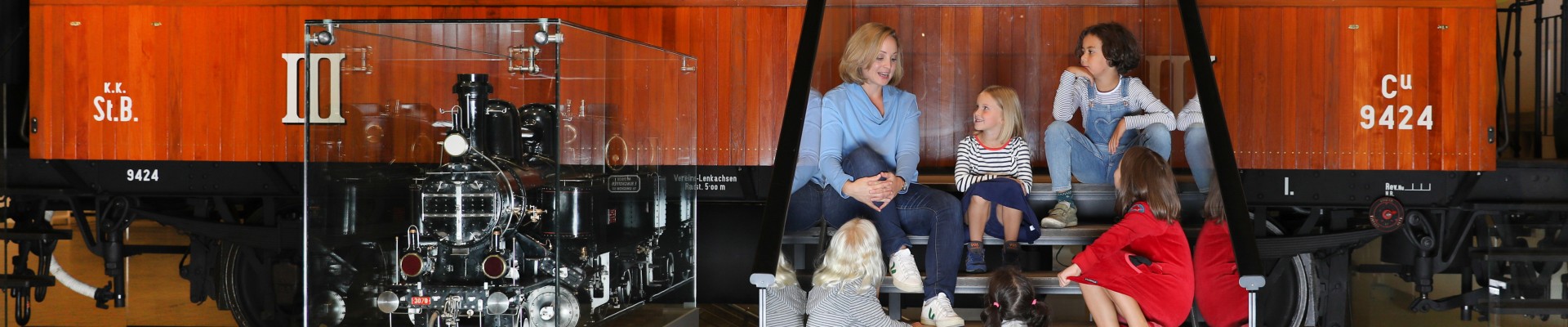 Children sit together with a tour guide on the stairs from Sisi´s Hofsalonwagen. It is part of the exhibition "Lok.Erlebnis" : 