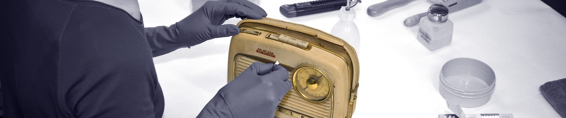 Black and white photo: museum employee working with a yellow transistor radio: 