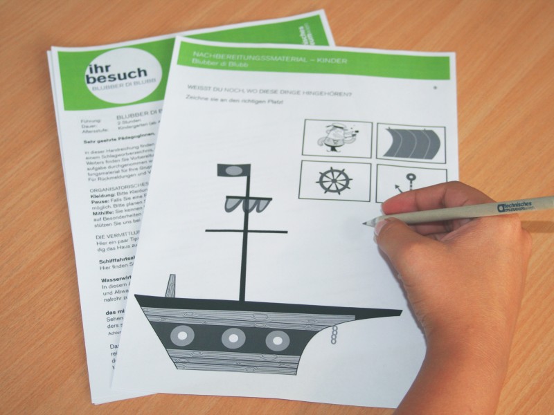 Kinderhand beim Ausfüllen eines Papierbogens, auf dem die Illustration eines Schiffes abgebildet ist.: 
