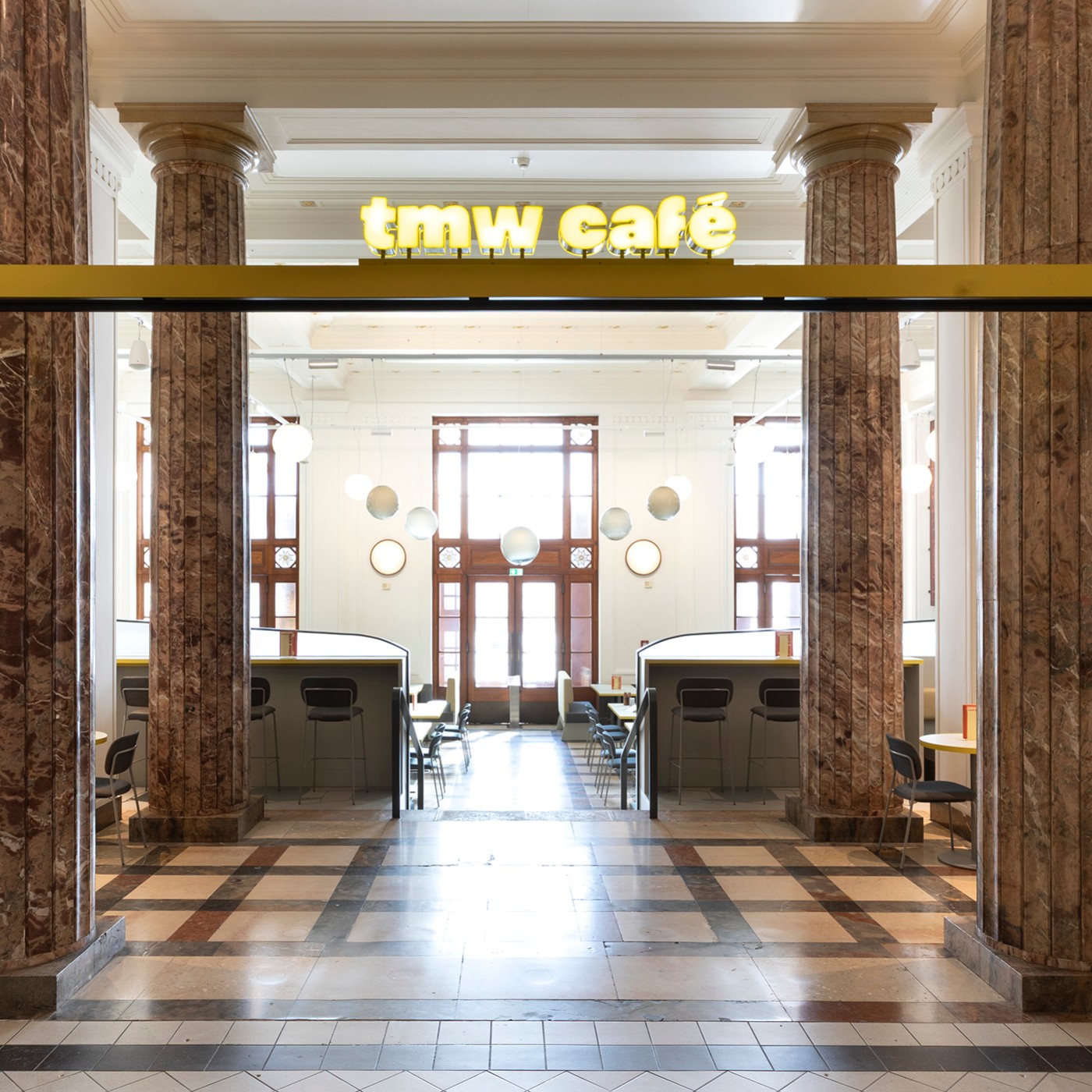 Entrance area of the tmw café at the Vienna Museum of Science and Technology, with a glowing yellow sign reading “tmw café” above the doorway: 