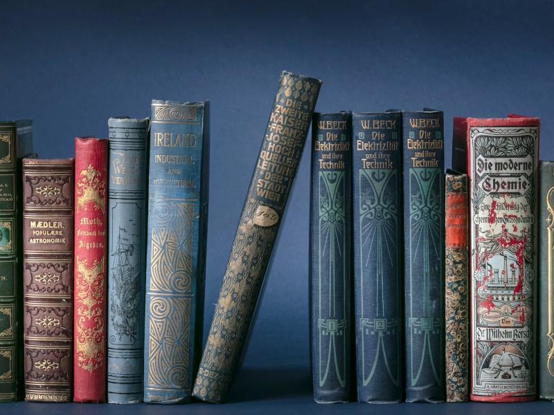Bunte Buchrücken historischer Publikationen vor einem blauen Hintergrund: 